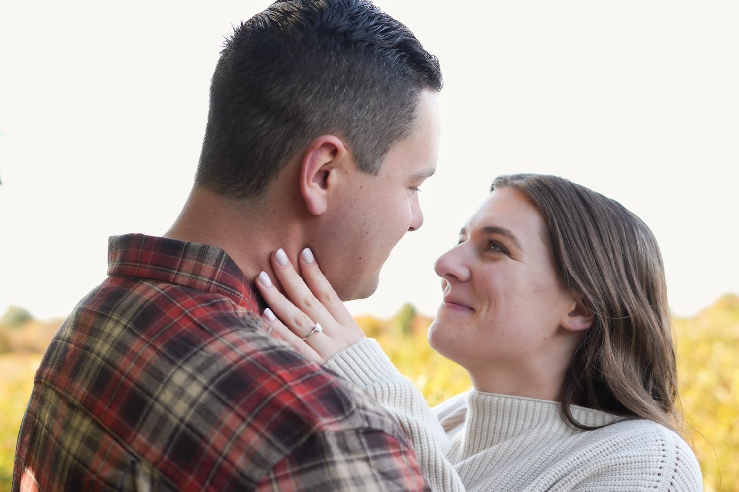 Newly engaged couple sharing a tender romantic moment in golden field.