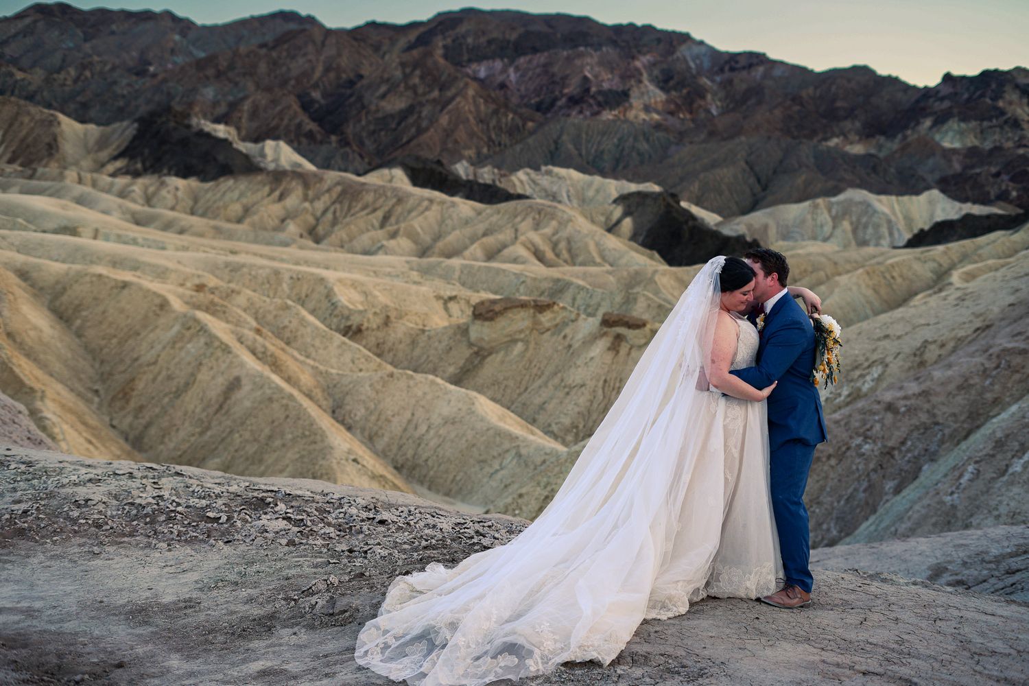 Bride and groom sharing romantic kiss at Zabriskie Point Death Valley with dramatic eroded hills.