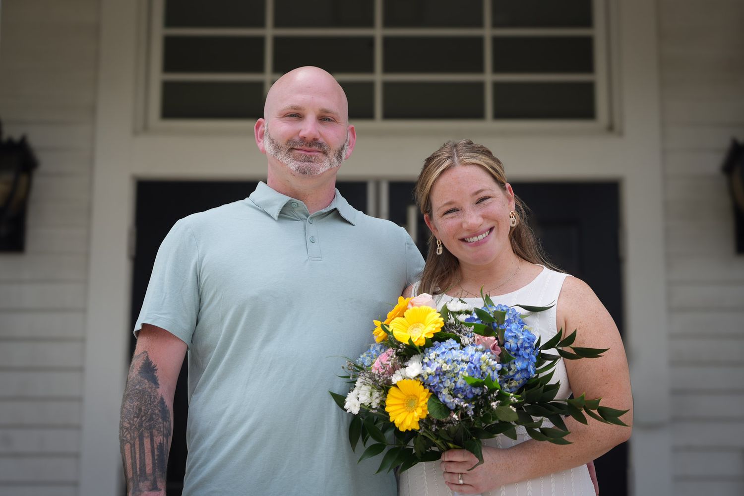 Smiling bride and groom posing together, bride holding yellow and blue wedding bouquet.