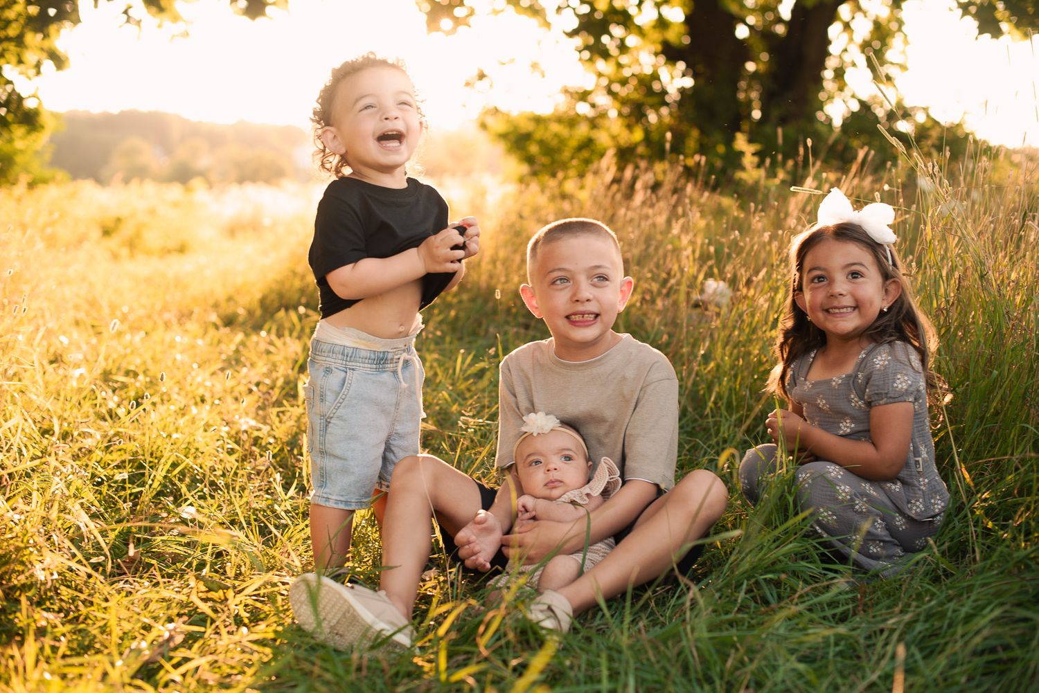 Four happy children sitting together in golden sunlit grass field smiling.