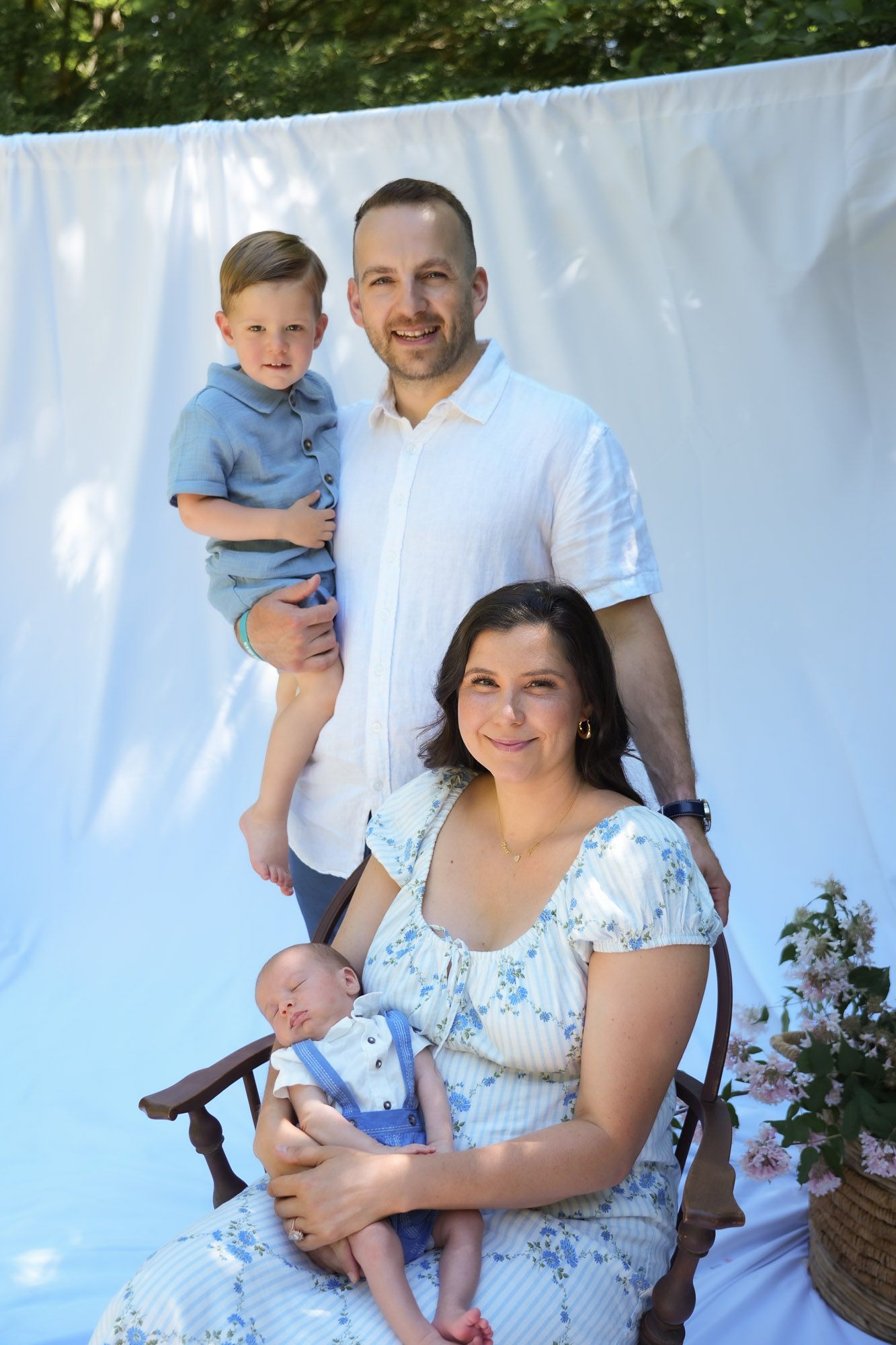 Family portrait with father holding toddler and mother cradling newborn outdoors.