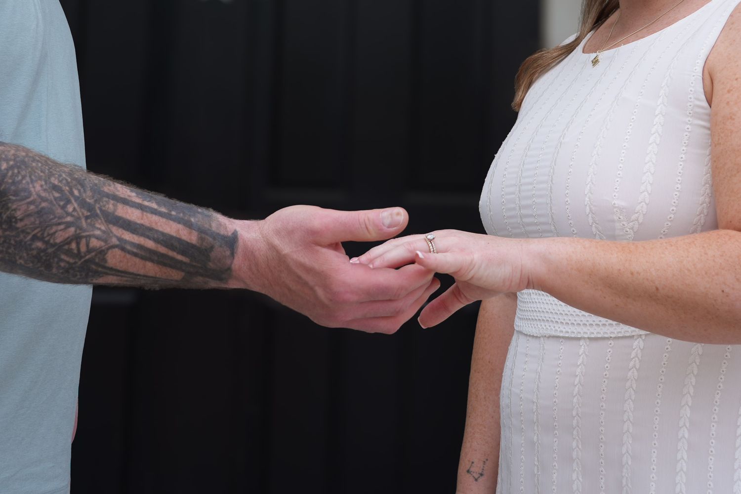 Close-up of tattooed groom placing wedding ring on bride's finger during intimate outdoor ceremony.