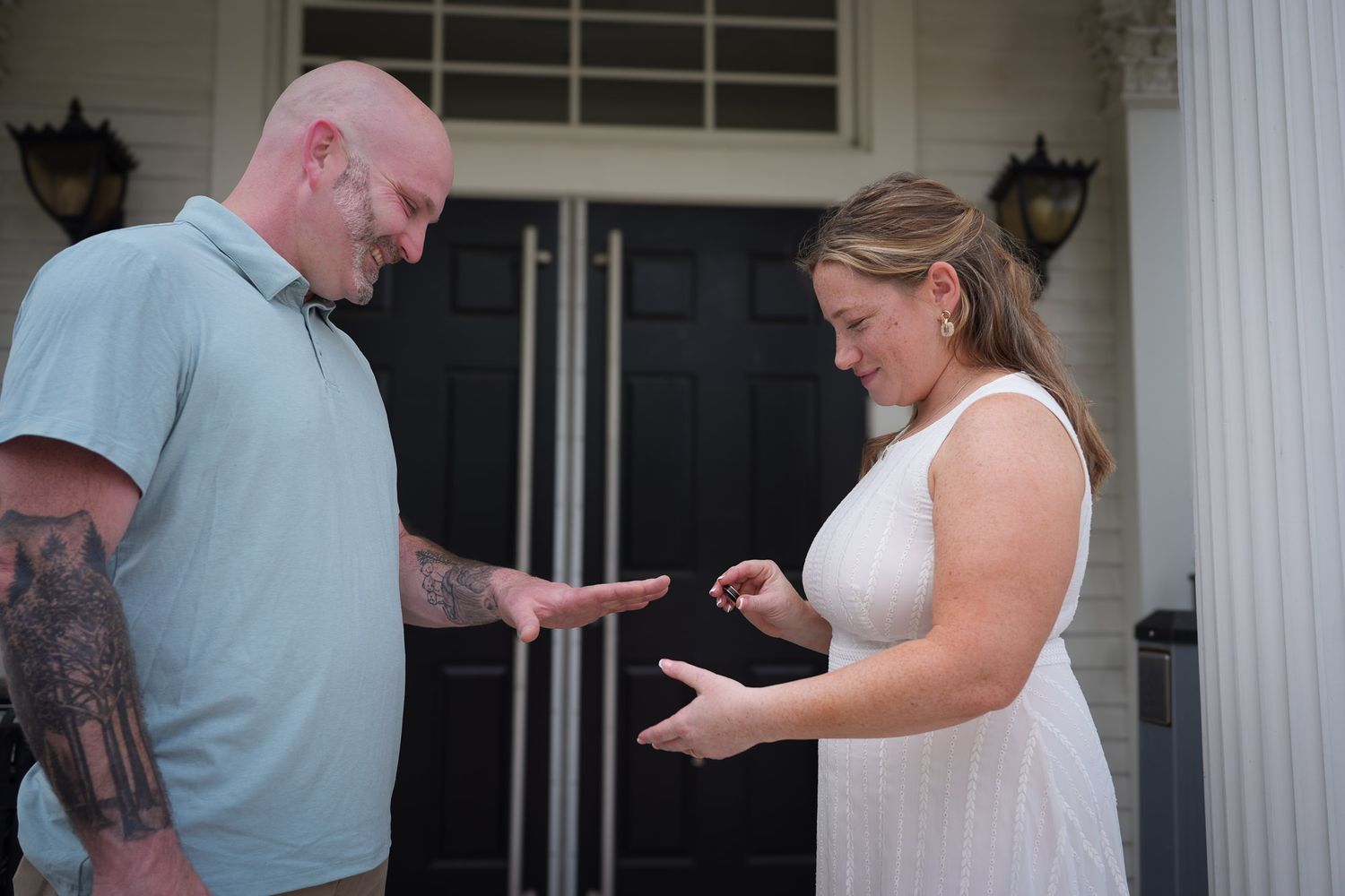 Couple bowing heads together during intimate ring exchange ceremony on white columned front porch.