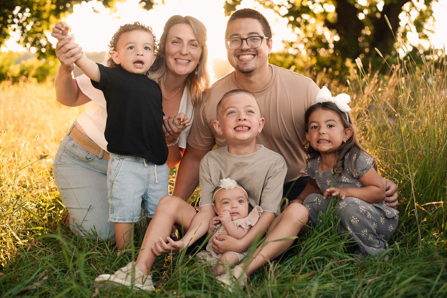 Happy blended family of six posing together in a golden sunlit field.