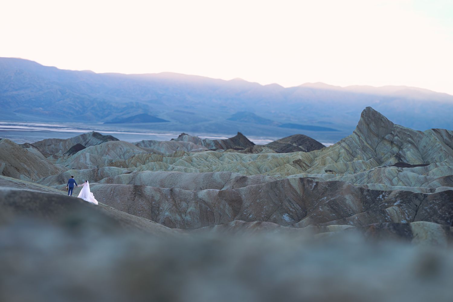 Bride and groom standing among dramatic rocky formations at Zabriskie Point in Death Valley at dusk.