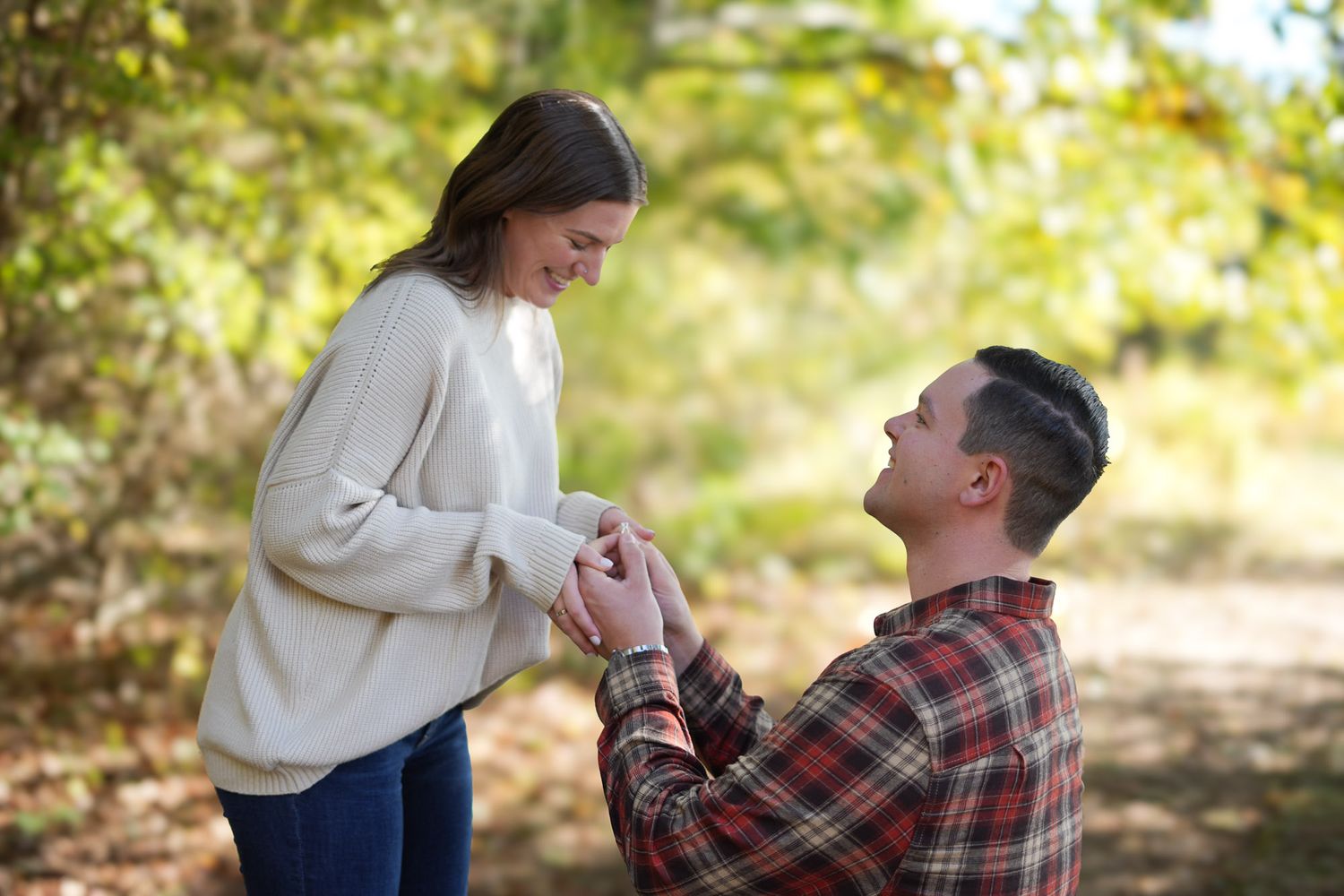 Man kneeling before smiling woman during outdoor fall engagement proposal.