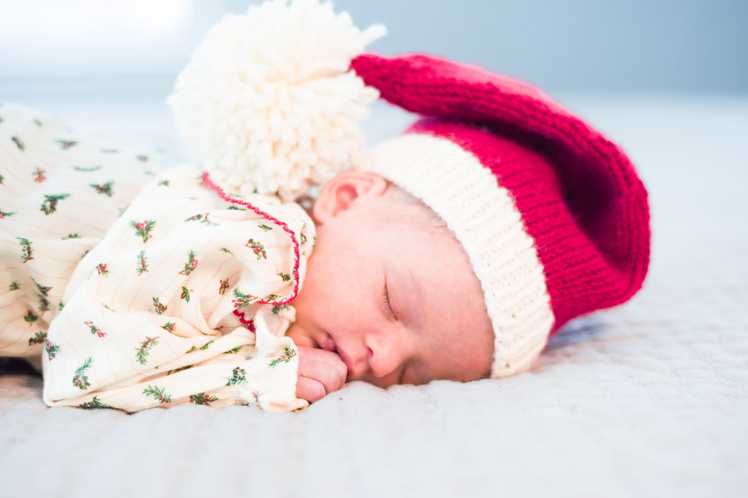 Newborn baby sleeping soundly in festive floral outfit with red and white pom-pom Santa hat.