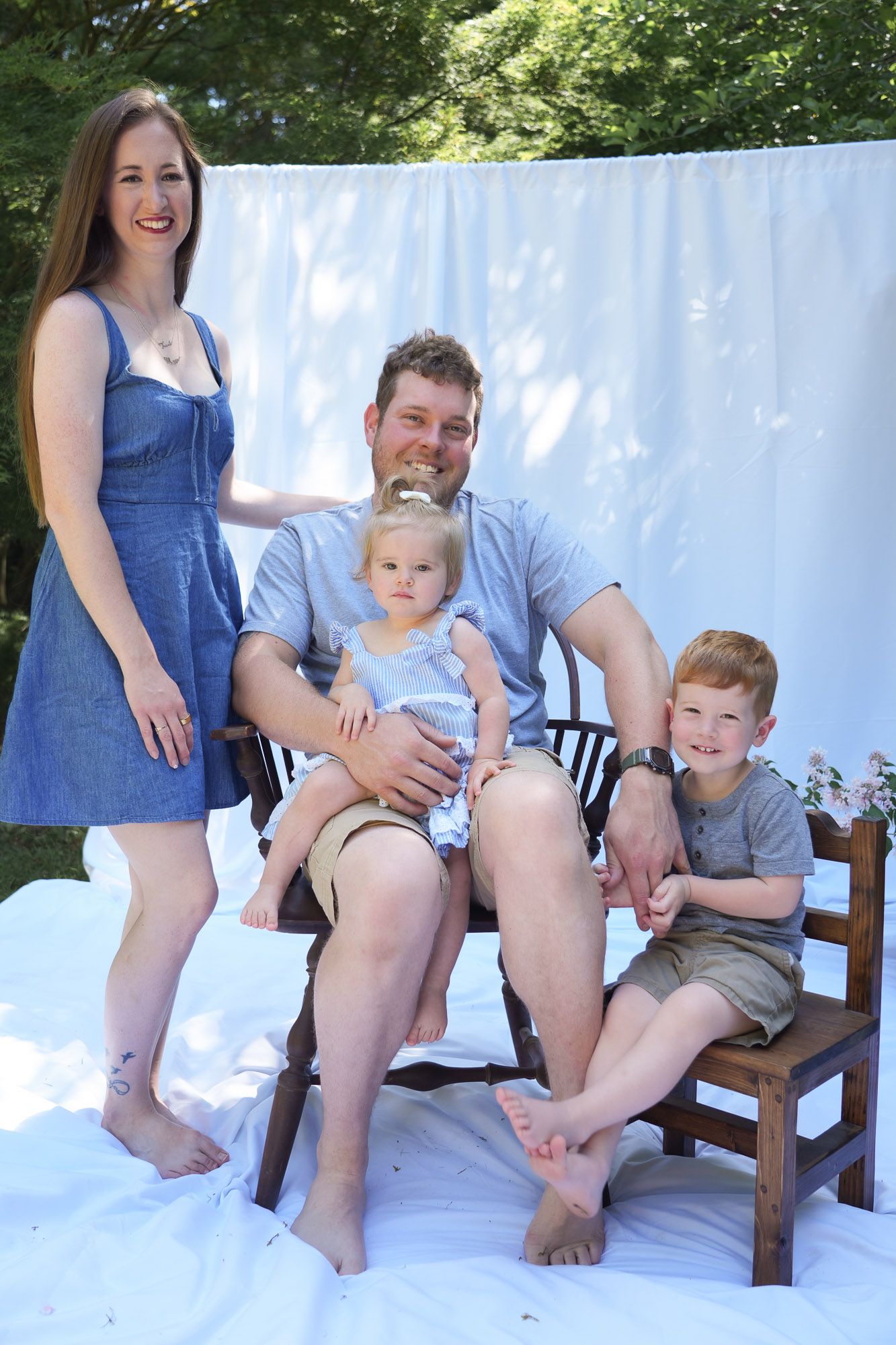 Happy family of four posing outdoors on white backdrop in casual summer clothing.