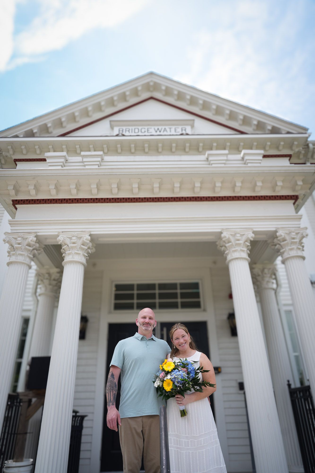 Wedding couple posing in front of Bridgewater building with bride holding yellow and blue bouquet.