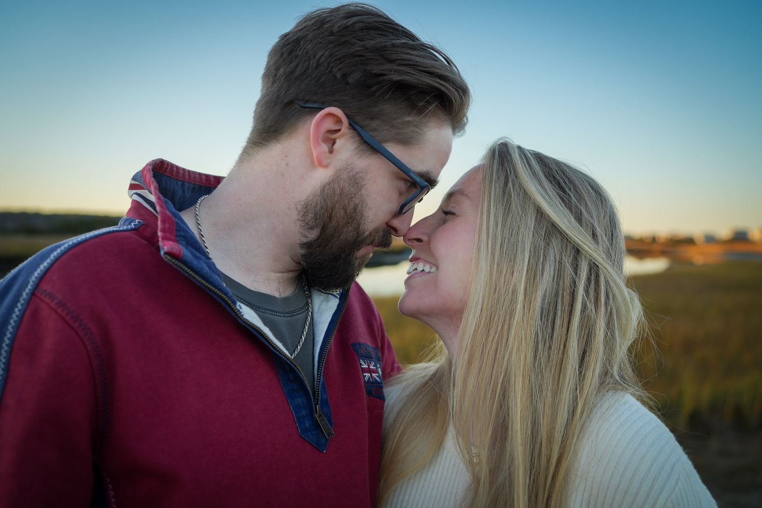 Close-up of smiling couple about to kiss outdoors at golden hour sunset.