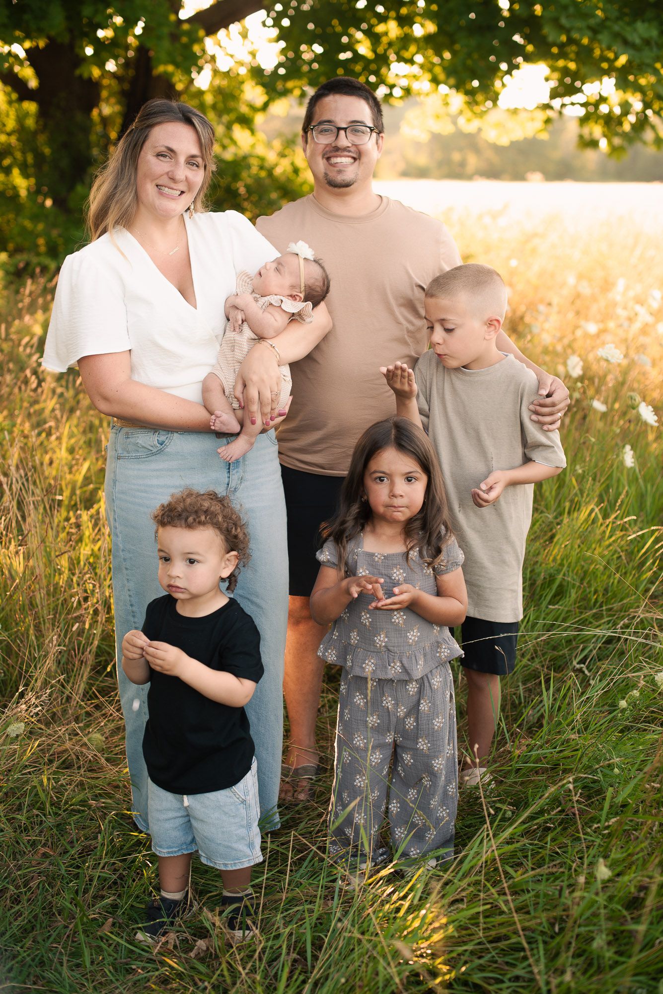 Happy family of six posing in golden sunlit meadow with newborn baby.