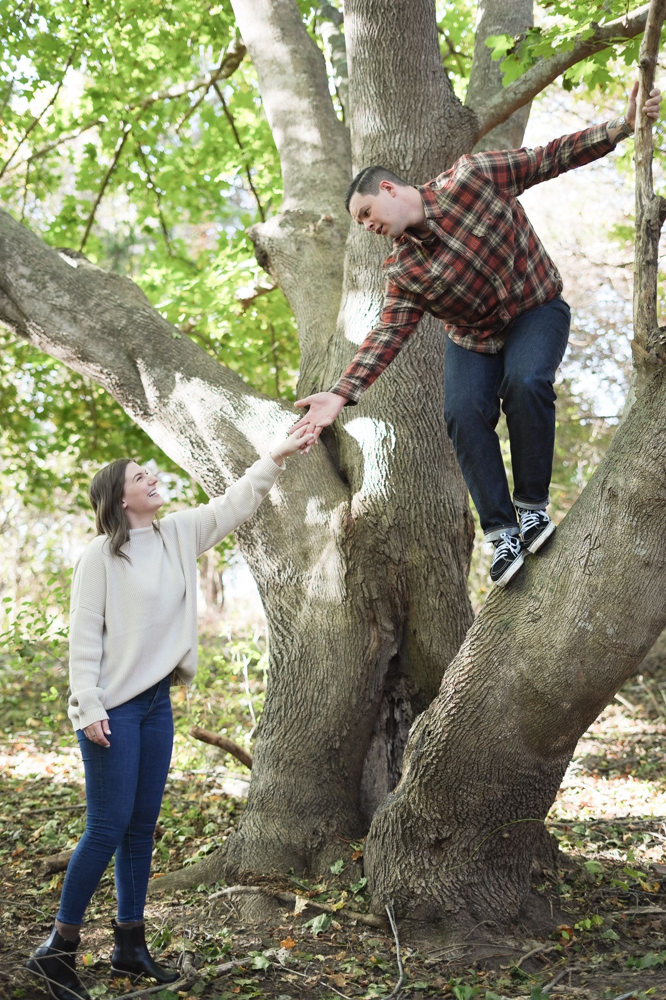 Woman reaching up to man climbing large tree in autumn forest.