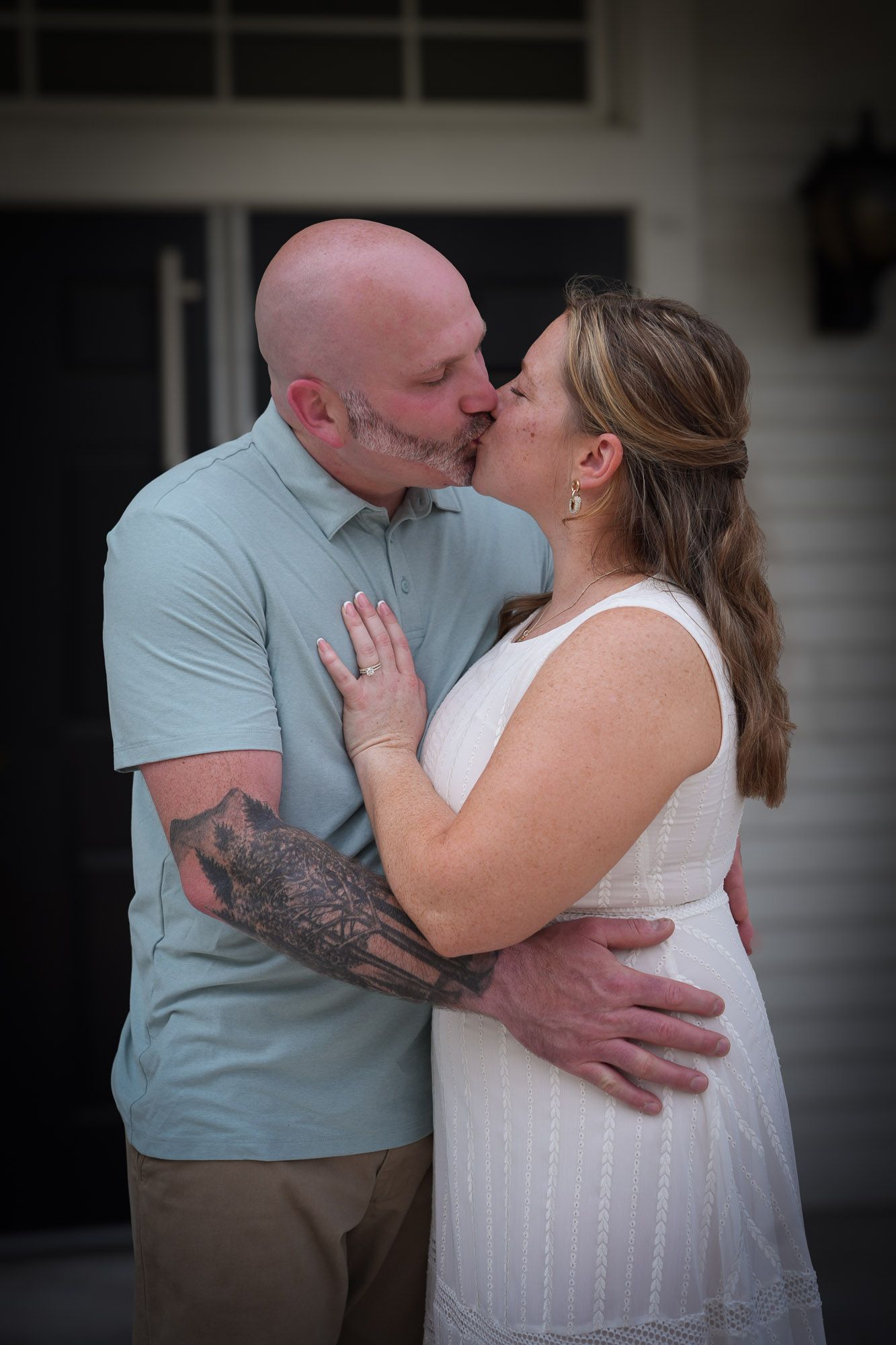 Newlyweds embracing and kissing, groom showing tattooed arms, bride in white dress.