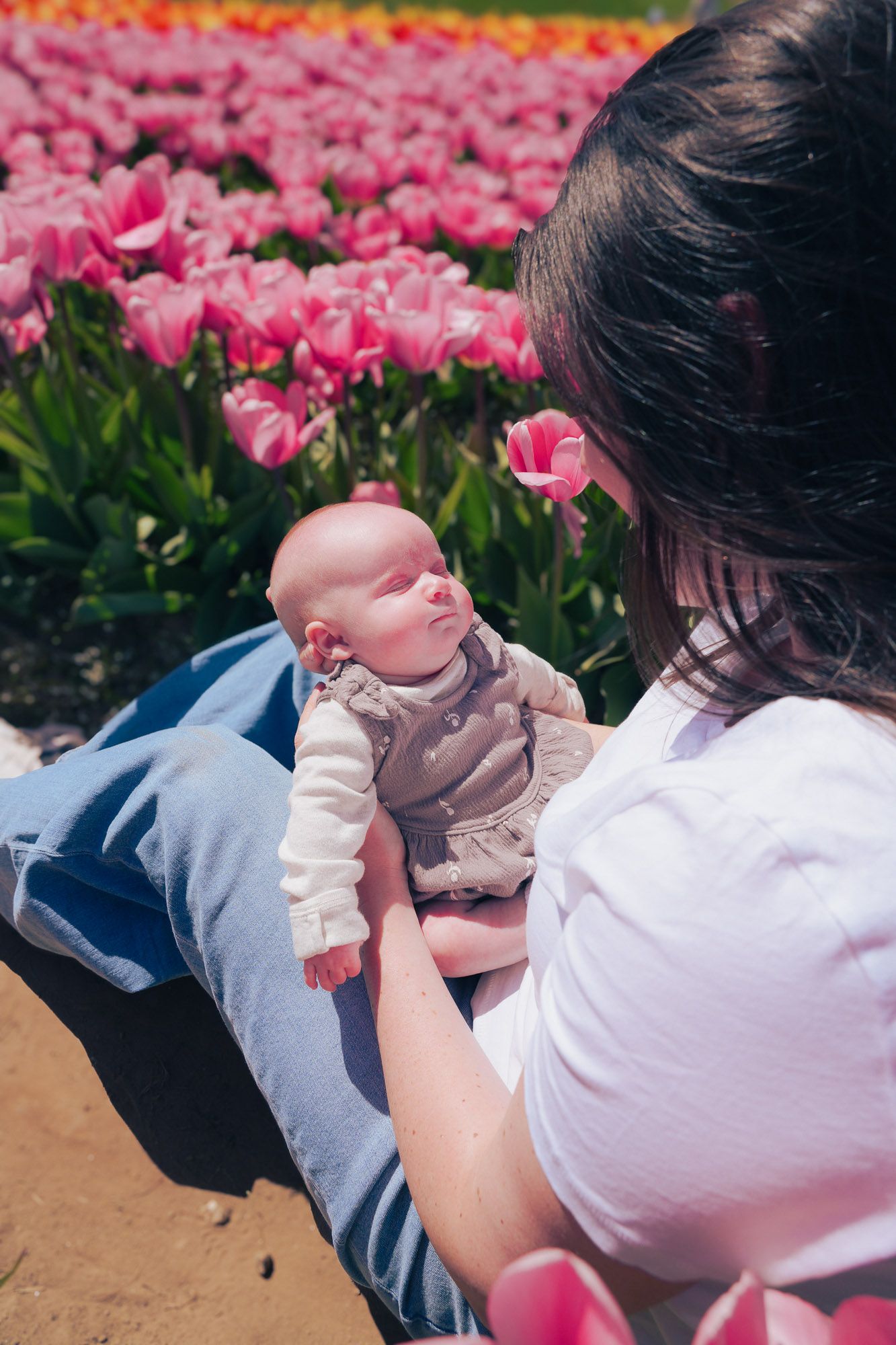 Mother holding sleeping newborn baby in a colorful tulip field.