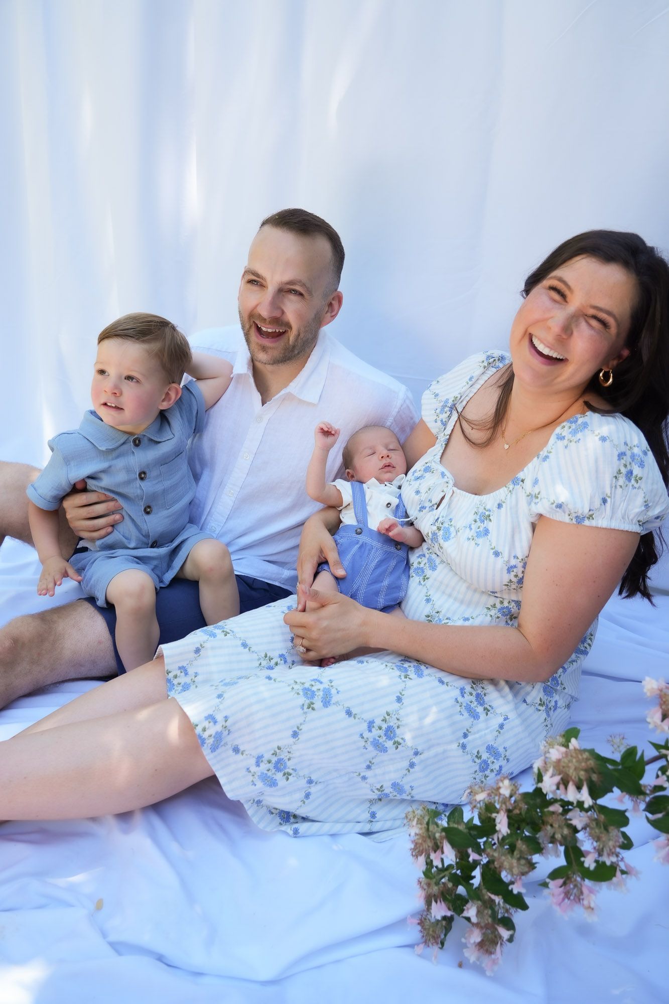 Happy family with newborn baby and toddler son laughing together on white backdrop.