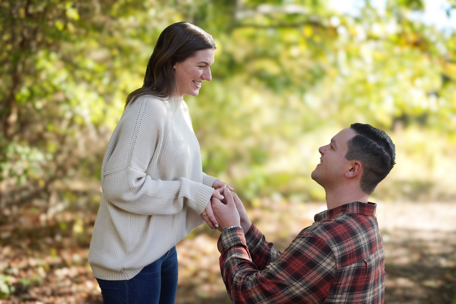 Joyful outdoor marriage proposal with couple in autumn forest setting.