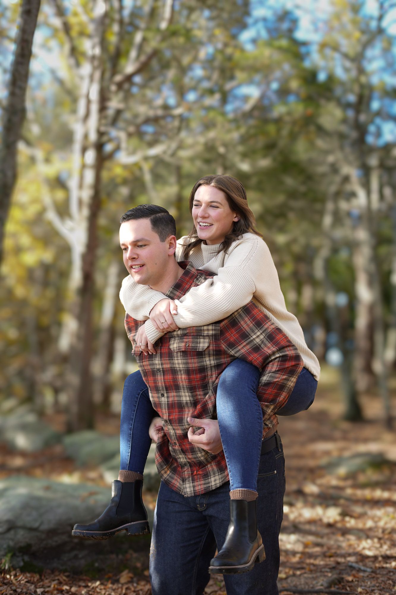 Man giving woman a piggyback ride through colorful autumn forest path.