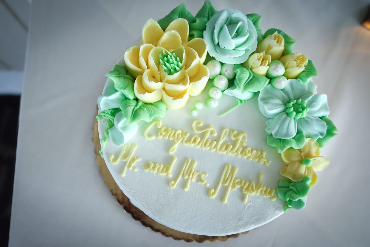 White wedding cake decorated with green and yellow buttercream flowers reading Congratulations Mr. and Mrs.