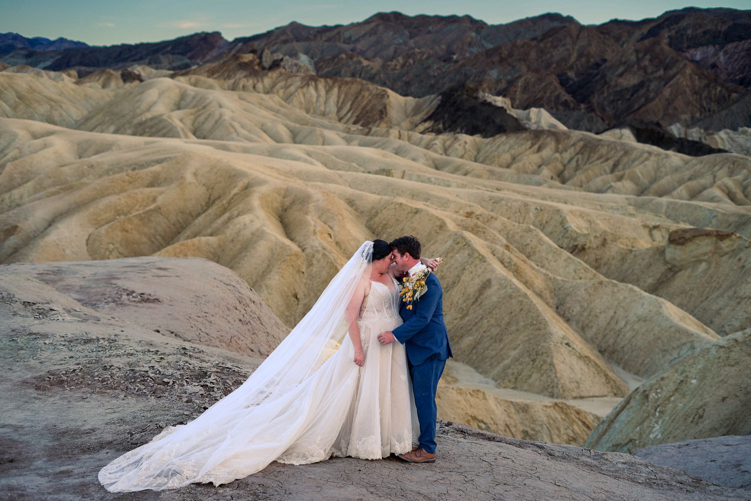 Bride and groom share a romantic kiss at Zabriskie Point in Death Valley with stunning eroded badlands behind them.