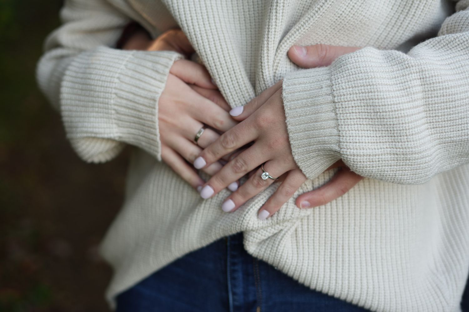 Close-up of hands with elegant rings and neutral manicure on a cozy cream knit sweater.