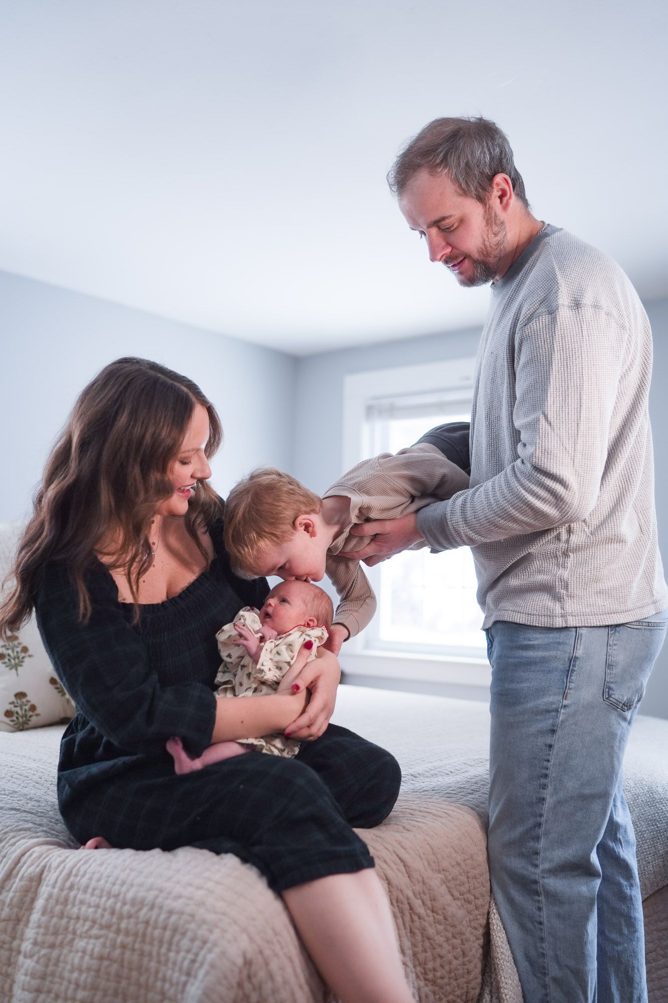 Happy family with toddler and newborn sharing a tender moment together on a bed.
