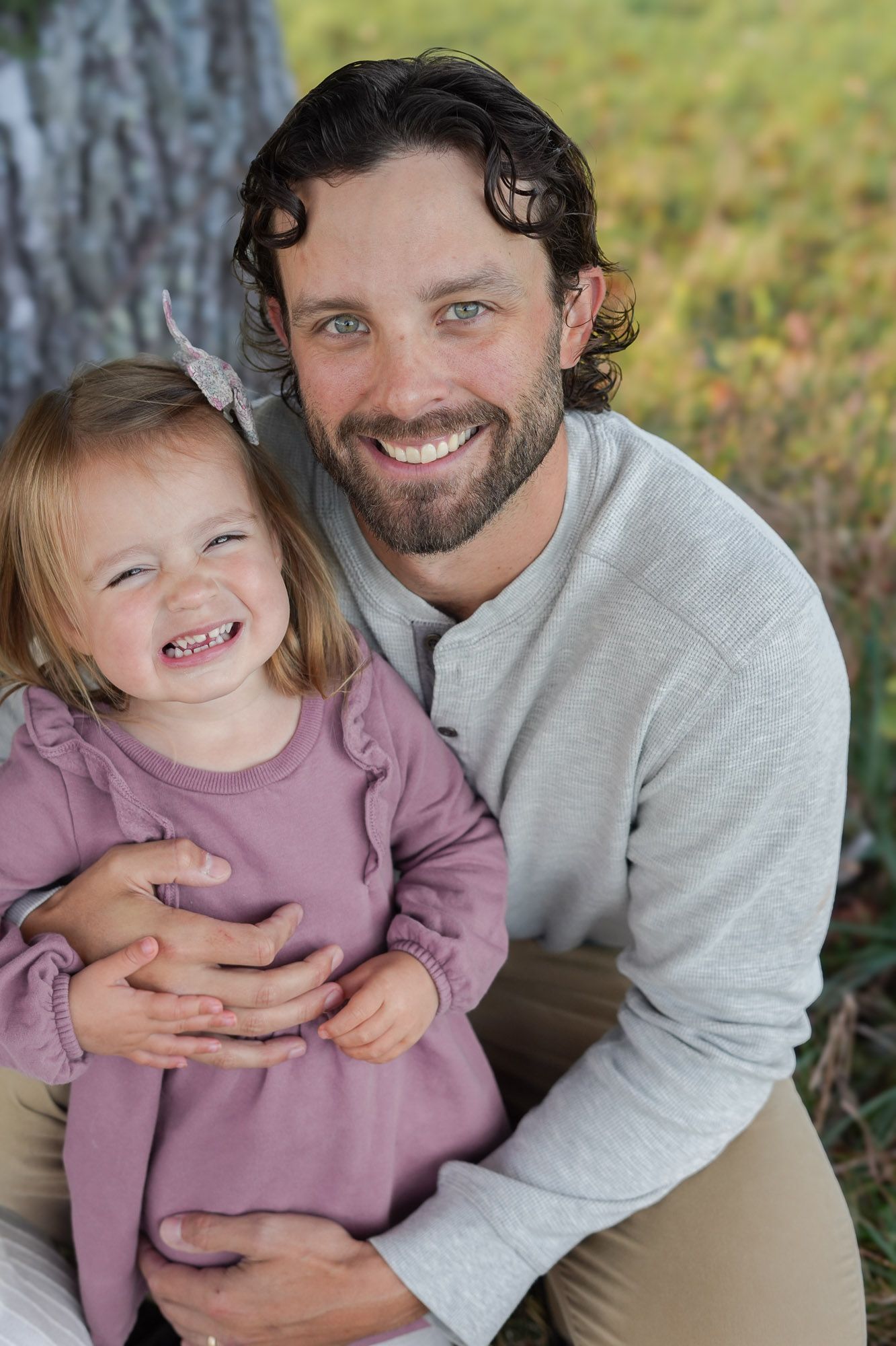 Smiling bearded father hugging his laughing toddler daughter outdoors near a tree in autumn.