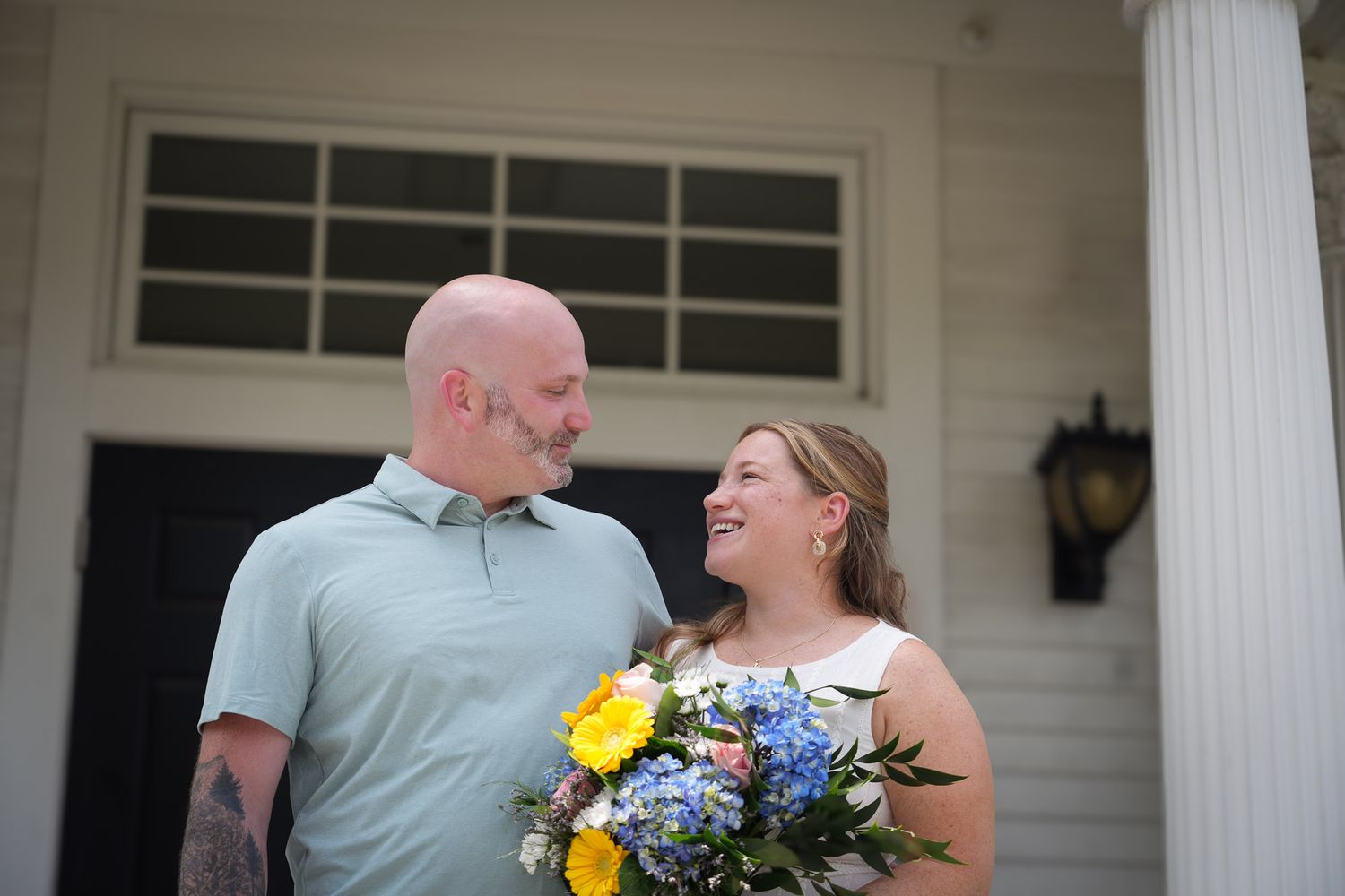 Happy wedding couple sharing a joyful moment, bride holding colorful floral bouquet outdoors.