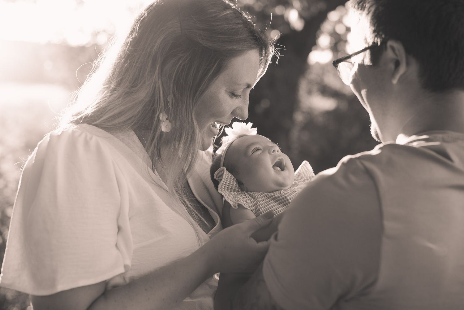 A black and white photo of loving parents gazing at their newborn baby in warm sunlight.