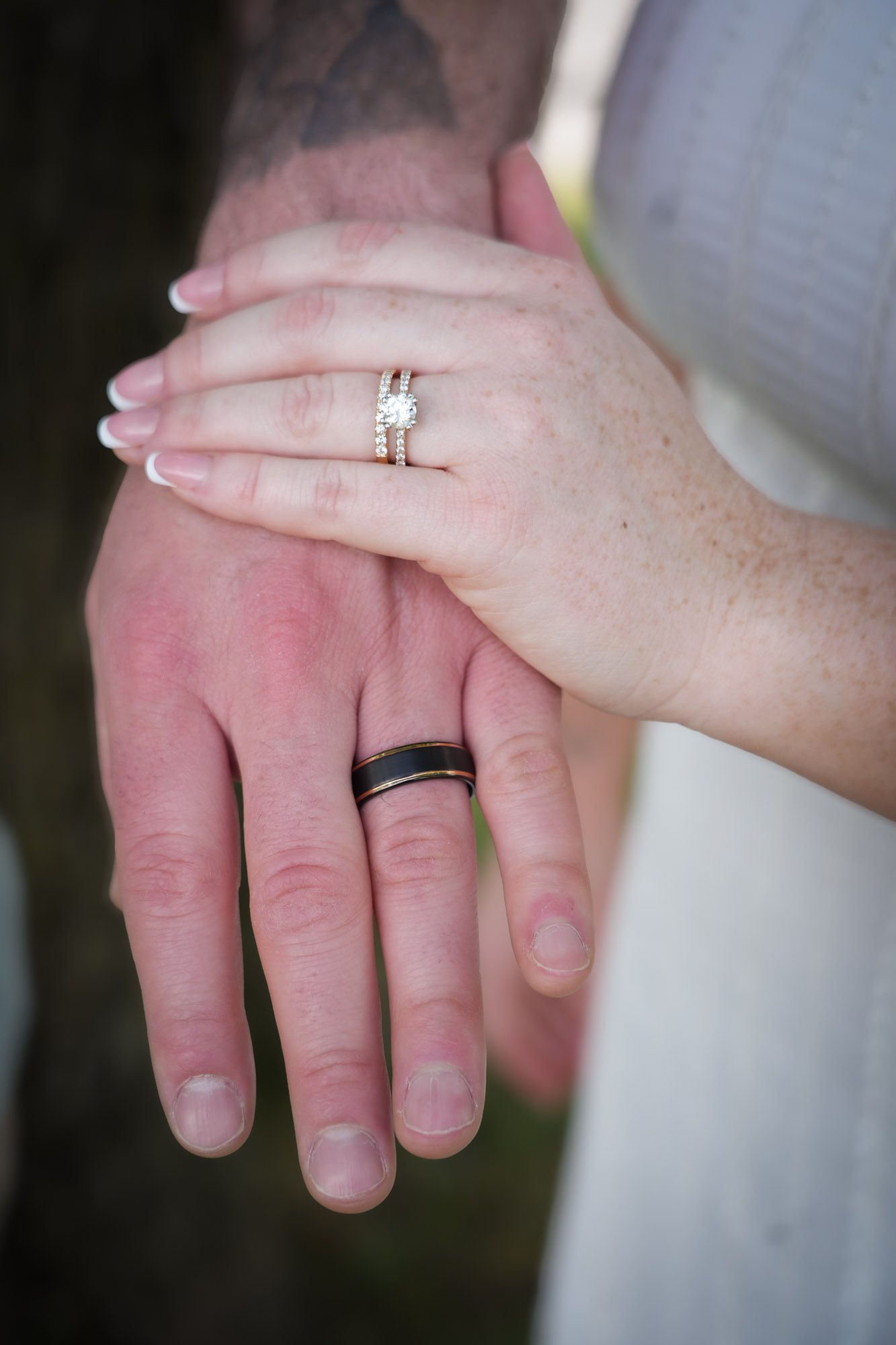 Couple displaying wedding rings, bride wearing diamond ring, groom wearing black band.