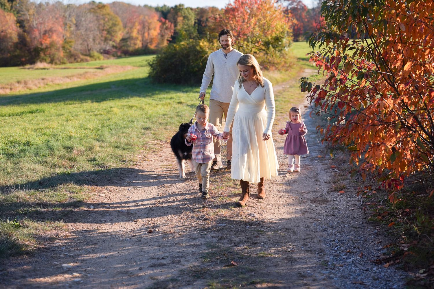 A family walks together on a scenic autumn path surrounded by colorful fall foliage.
