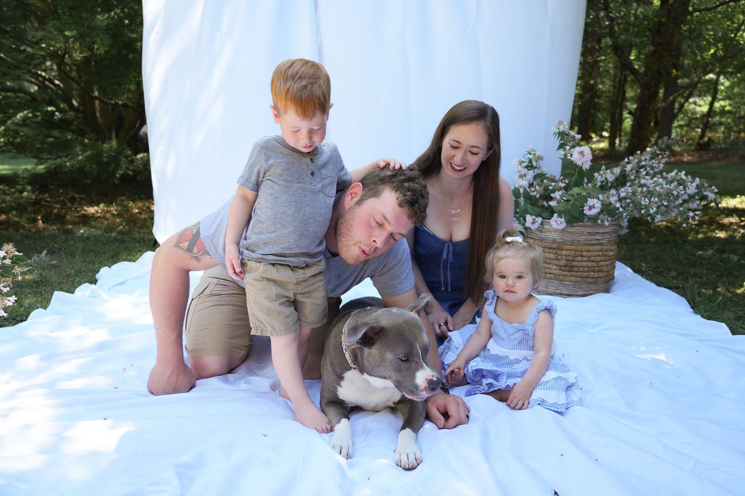 Happy family with two young children and gray dog on white blanket outdoors.