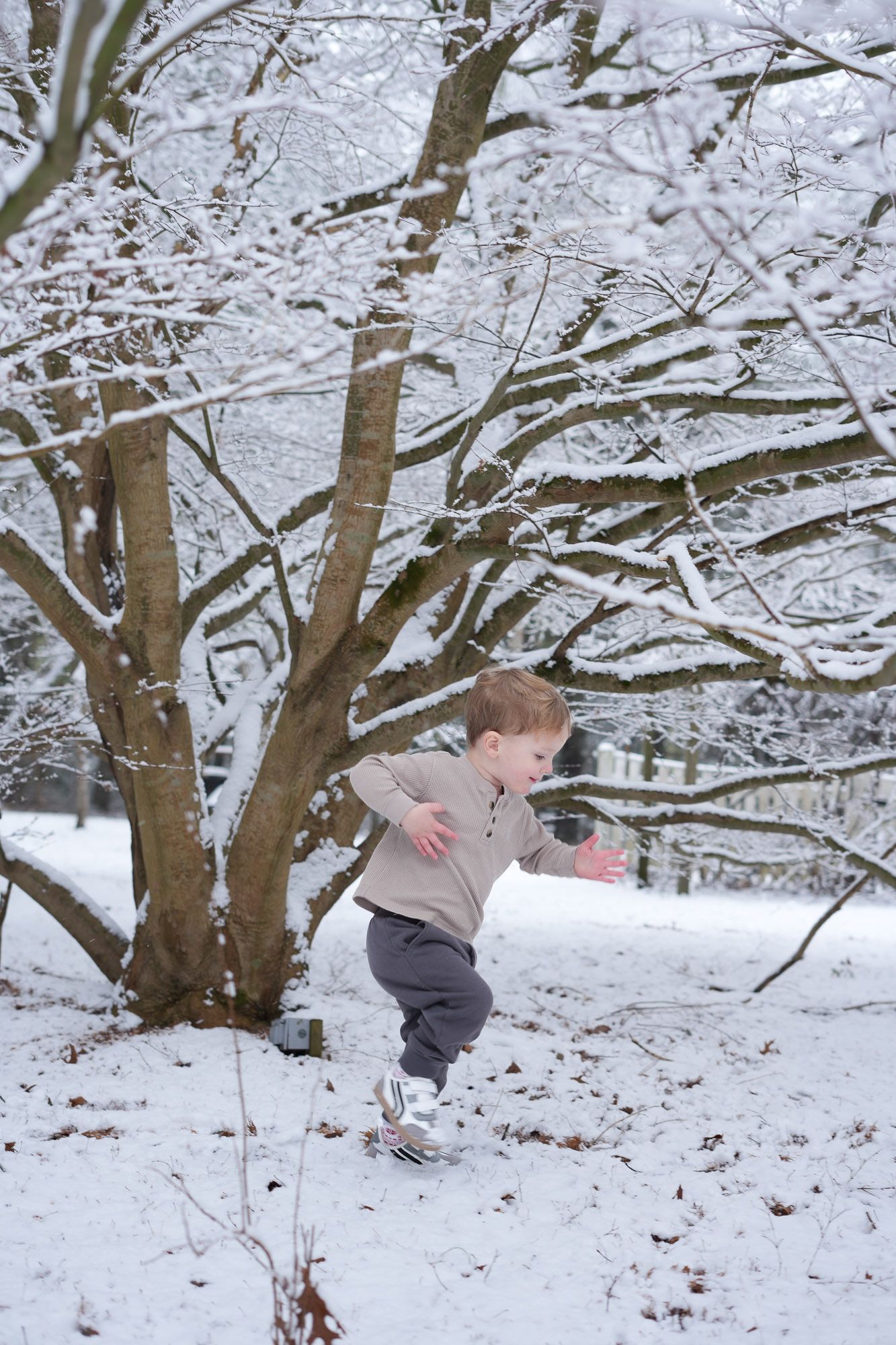 Young boy running and playing in a snowy winter park with snow-covered trees in the background.