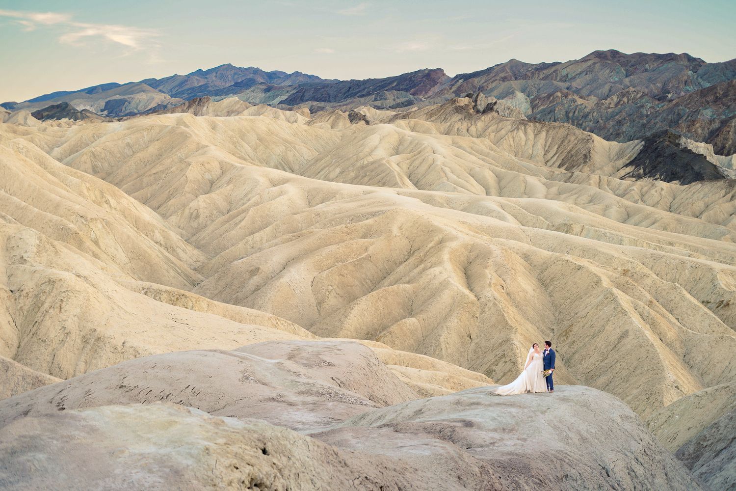 Wedding couple stands together on a ridge at Zabriskie Point surrounded by vast golden desert landscape in Death Valley.