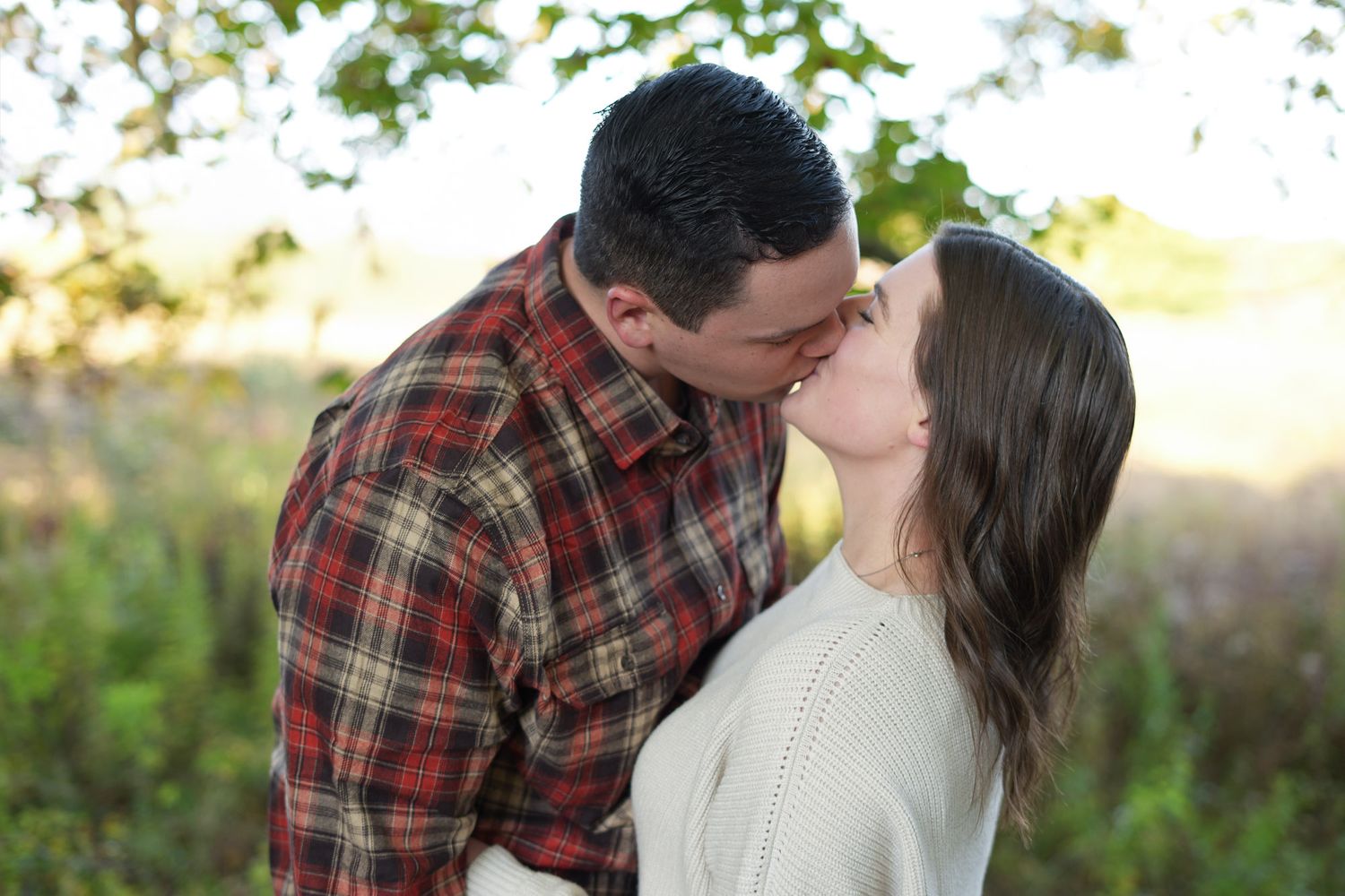 Couple sharing a romantic kiss outdoors surrounded by golden autumn foliage at sunset.
