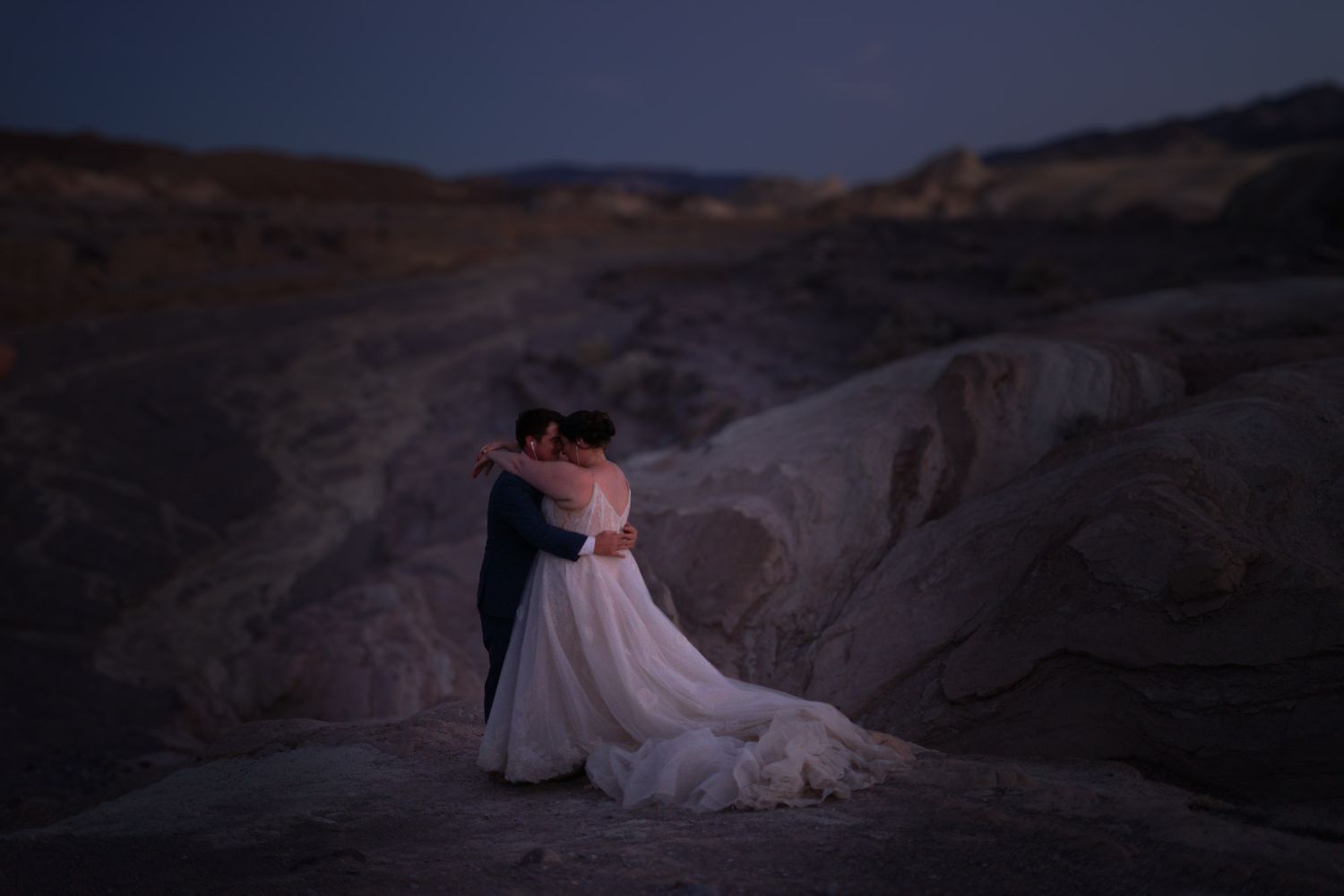 Wedding couple sharing a romantic embrace at night in a dramatic desert rock landscape.