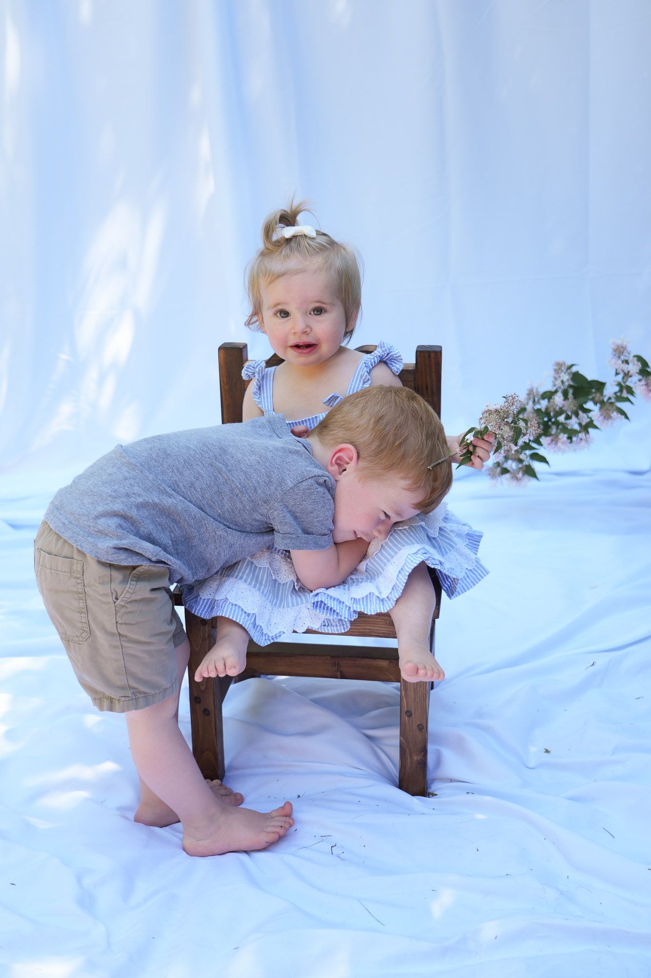 Two young siblings playing together on small wooden chair during outdoor photo session.