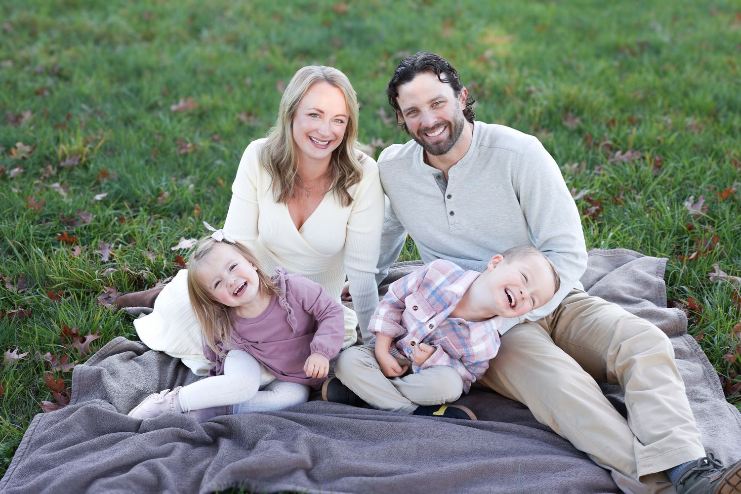 Cheerful family of four relaxing on a blanket outdoors, with young boy lying down laughing.