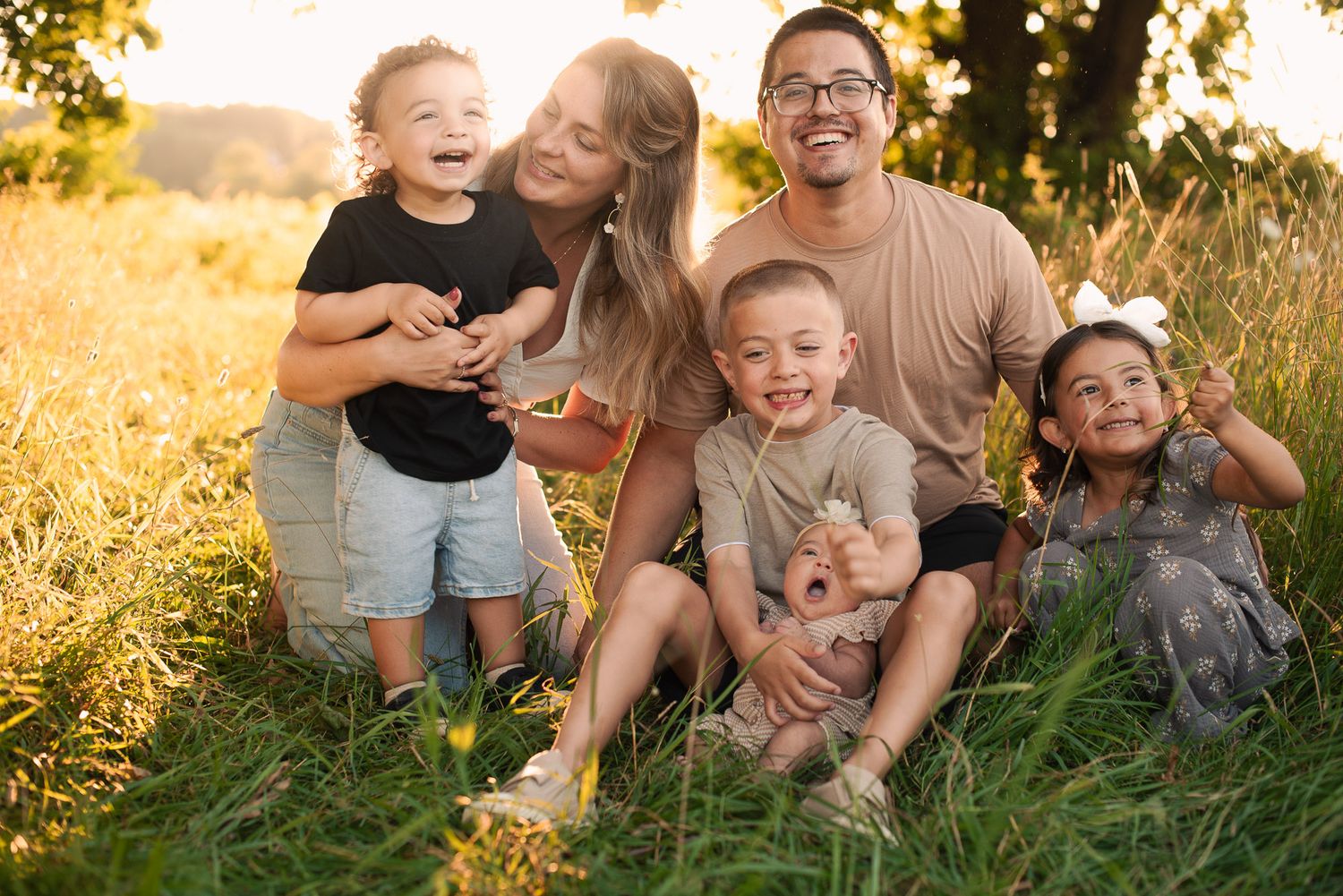 Joyful family of six sitting together in a sunny golden meadow.