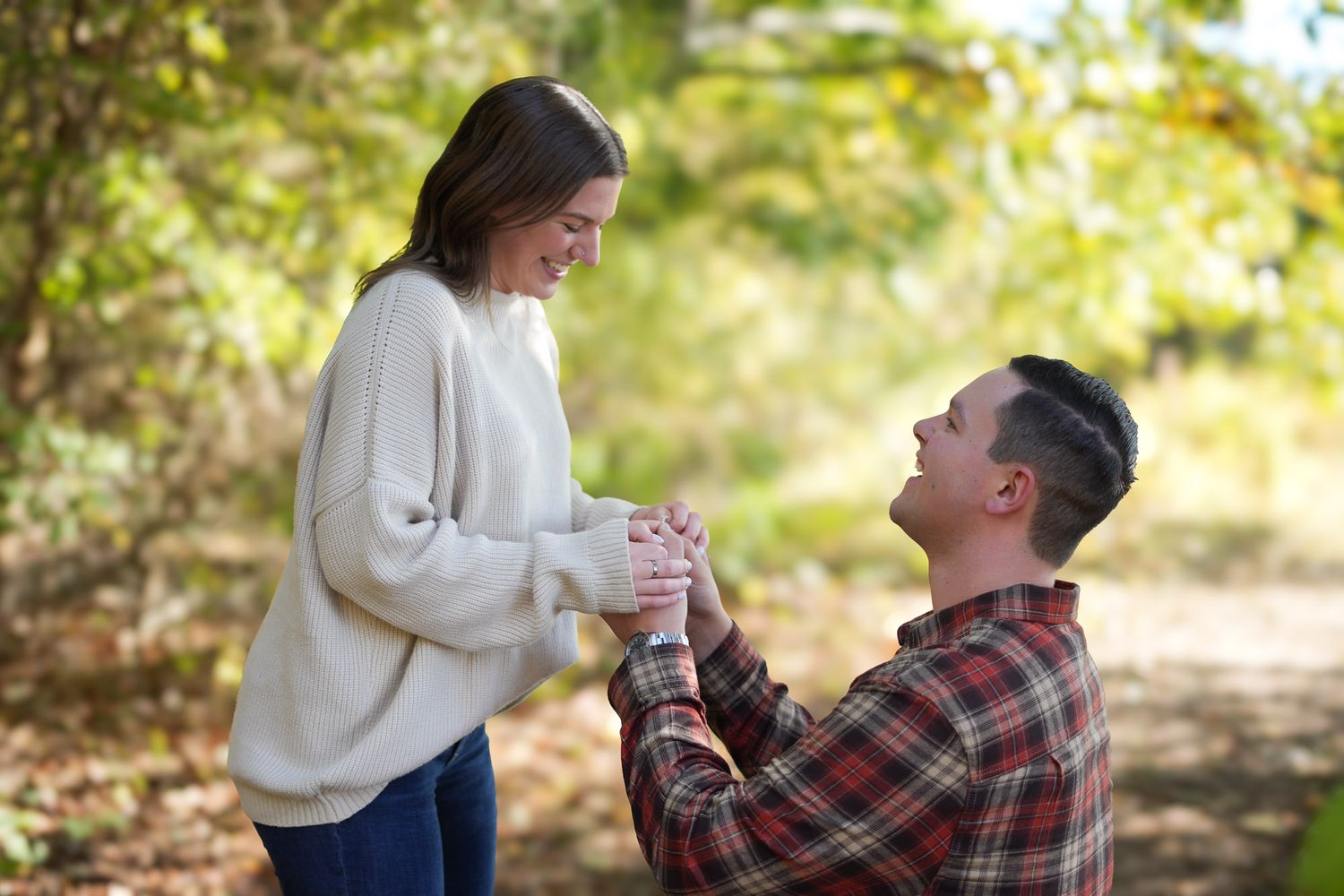 Happy couple sharing romantic proposal moment in sunlit autumn woods.