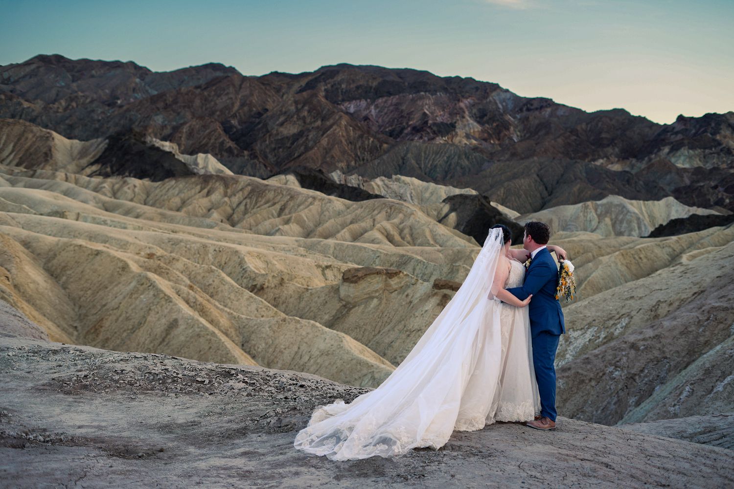 Bride and groom share romantic moment at Zabriskie Point with sweeping Death Valley landscape behind.