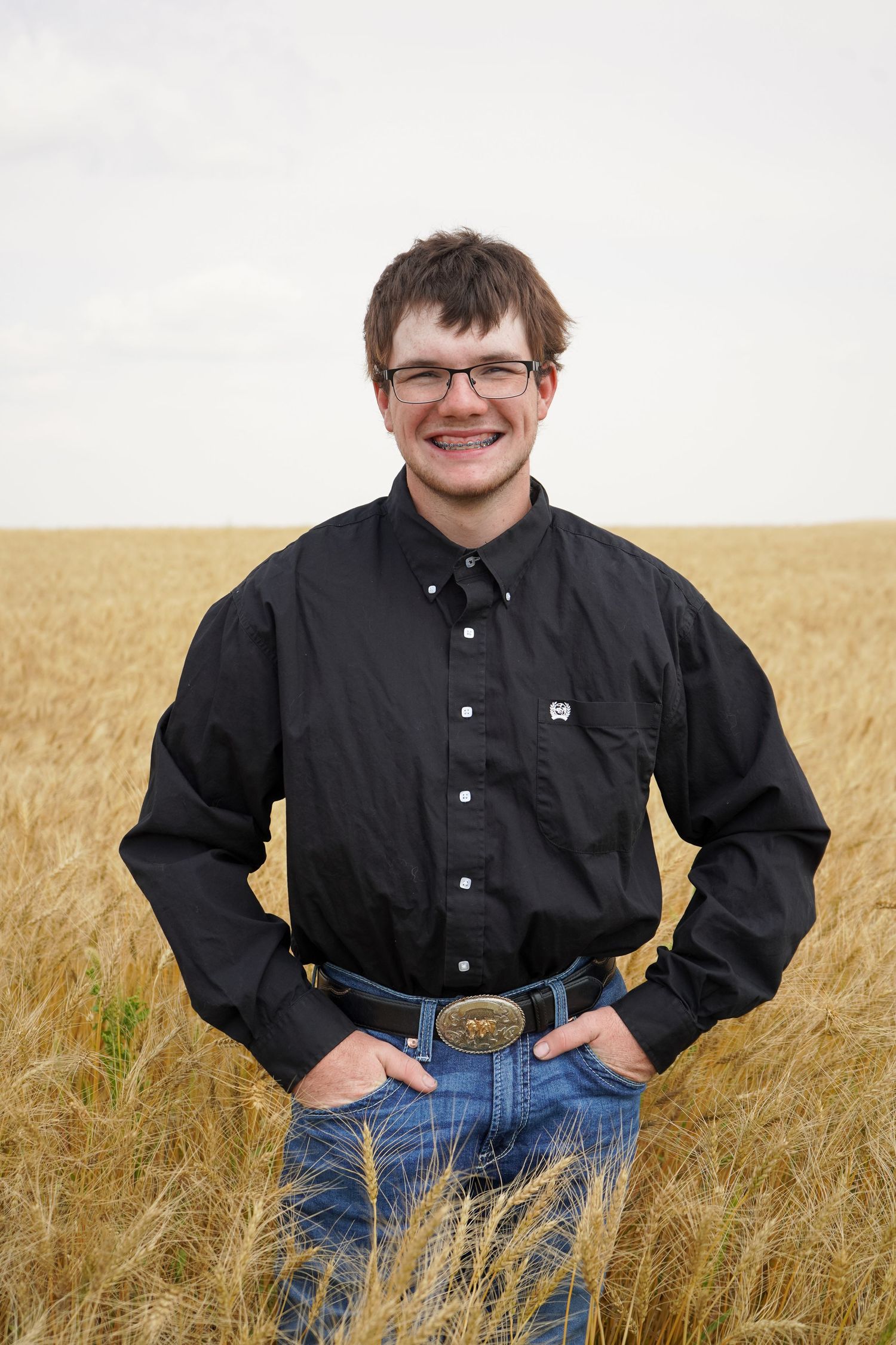 Smiling young man in black shirt and jeans standing in golden wheat field.
