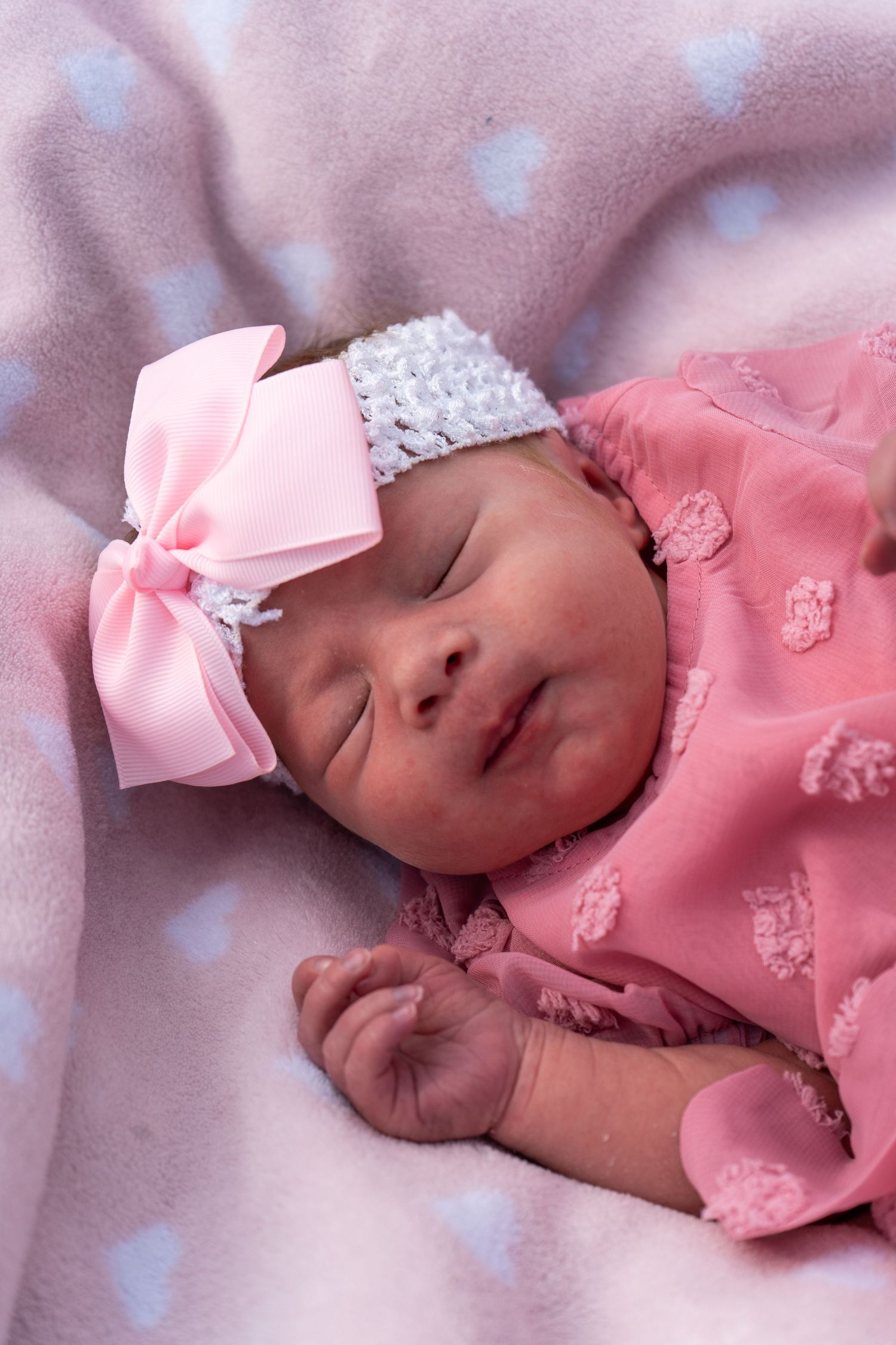 Peaceful newborn baby girl sleeping in pink outfit with pink bow headband.