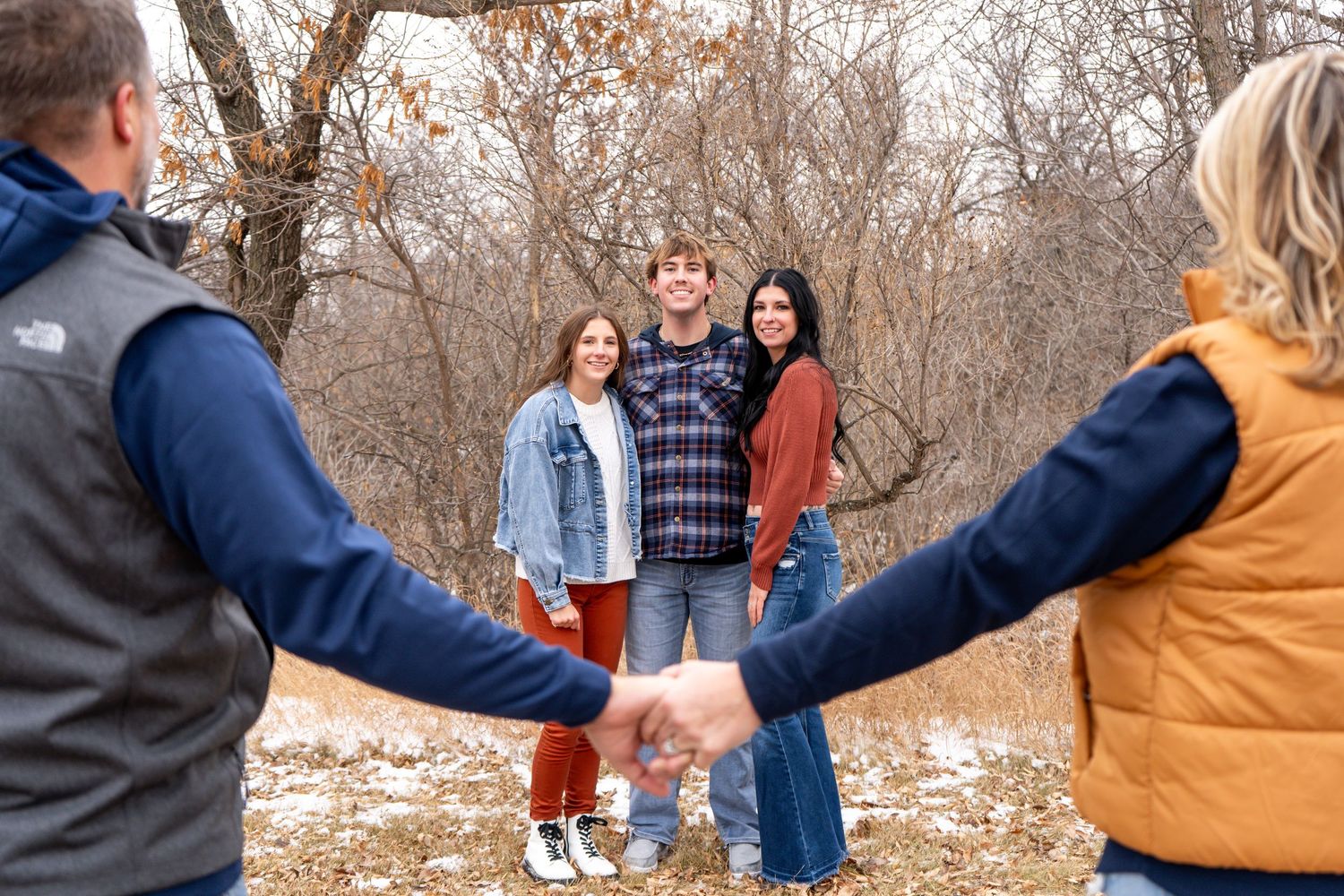 Two adults holding hands in foreground framing three young adults posing in winter landscape.
