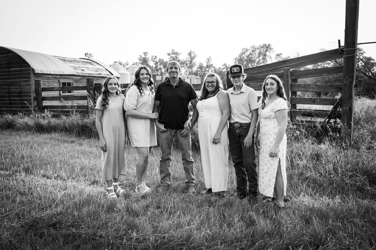 Black and white family portrait of six people standing in rustic farm field setting.