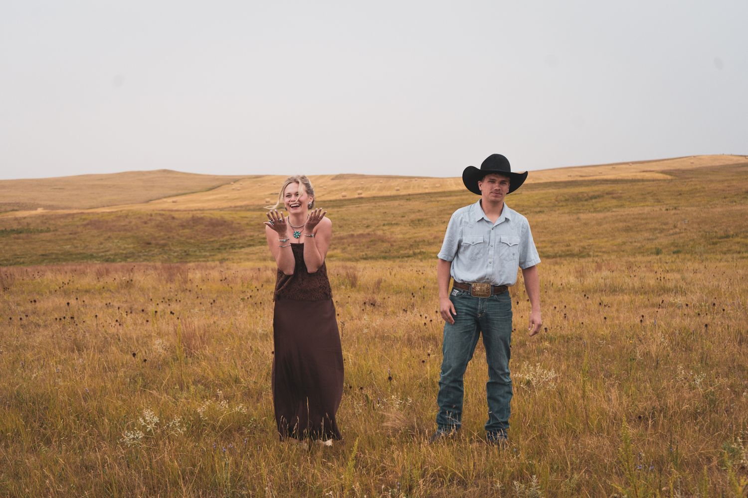Woman with hands on face in joyful surprise after proposal in expansive golden prairie landscape.