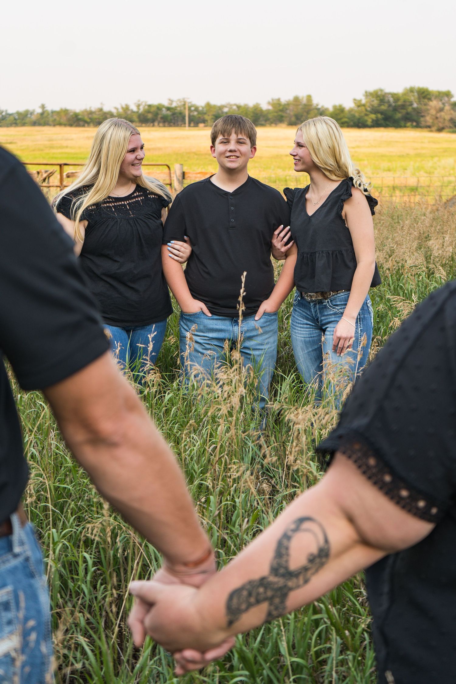 Three teens standing in tall grass field while parents hold hands in foreground.