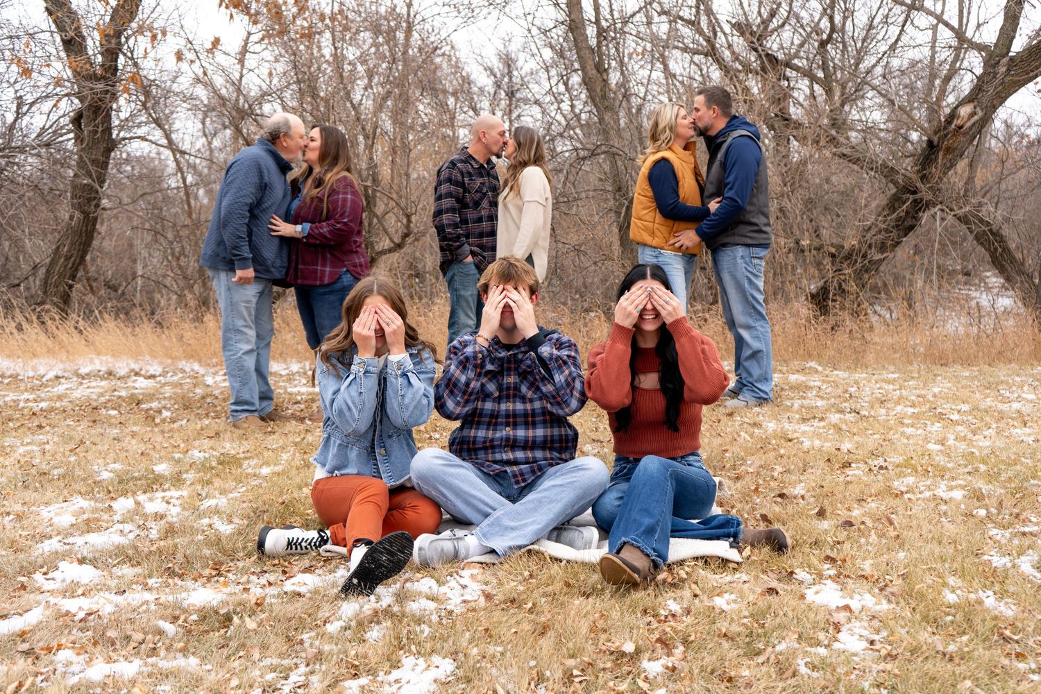 Fun family photo with couples kissing in background while three people cover eyes in foreground.