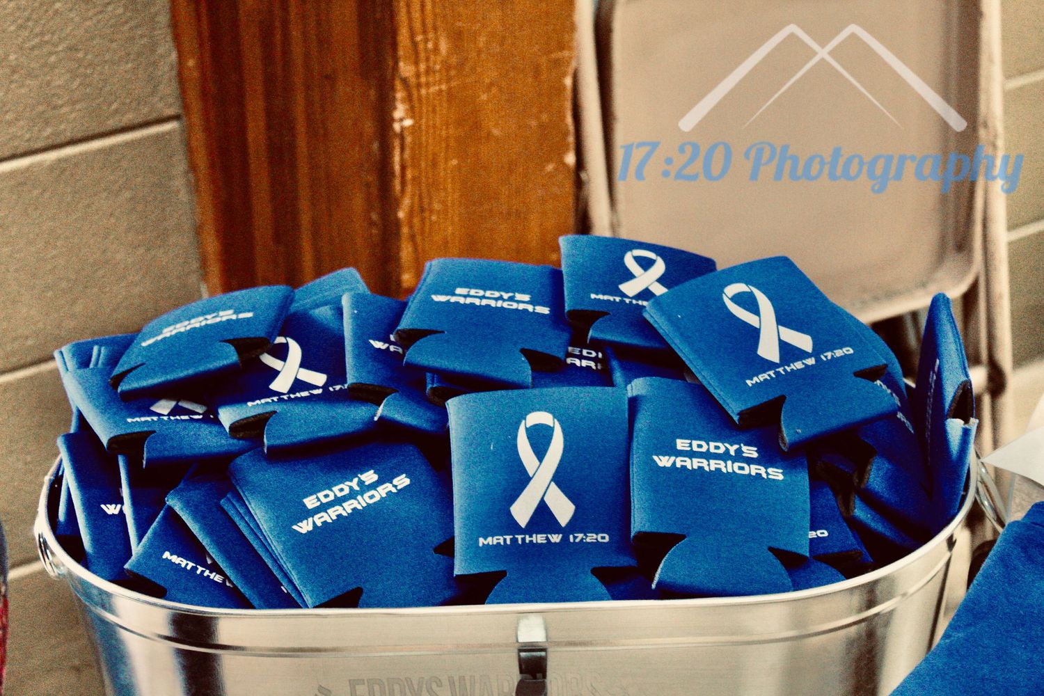 Bucket filled with blue Eddy's Warriors koozies featuring a white awareness ribbon and Matthew 17:20.