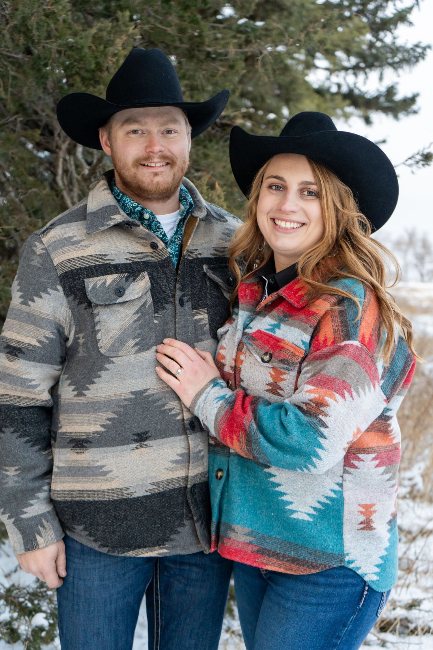 Smiling couple in matching Aztec print jackets and black cowboy hats posing in a snowy outdoor setting.