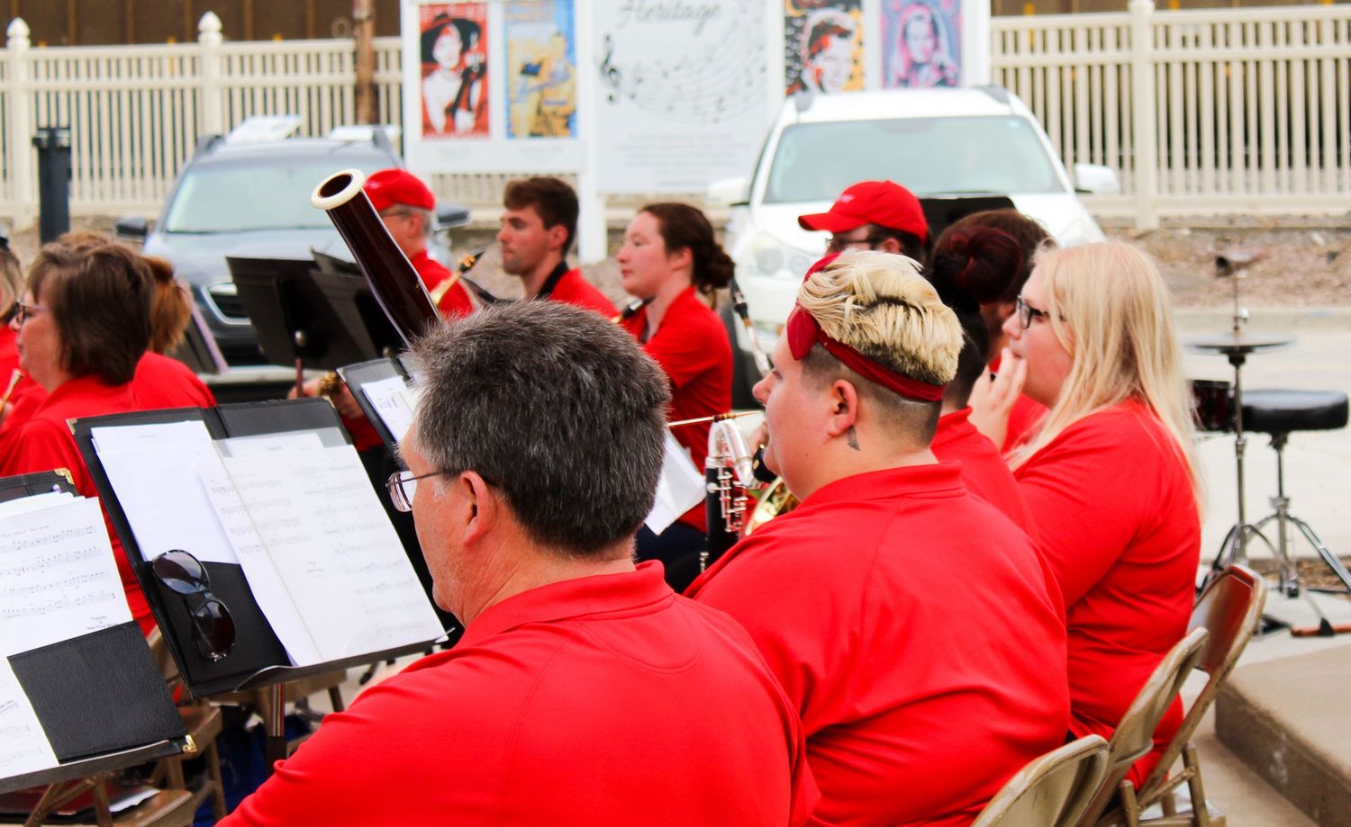 Musicians in red uniforms reading sheet music at an outdoor community band concert performance.